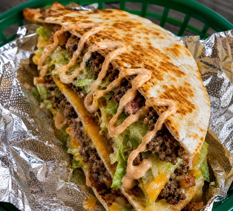 Three crispy tacos filled with seasoned ground beef, melted cheese, lettuce, and topped with creamy sauce on a green tray