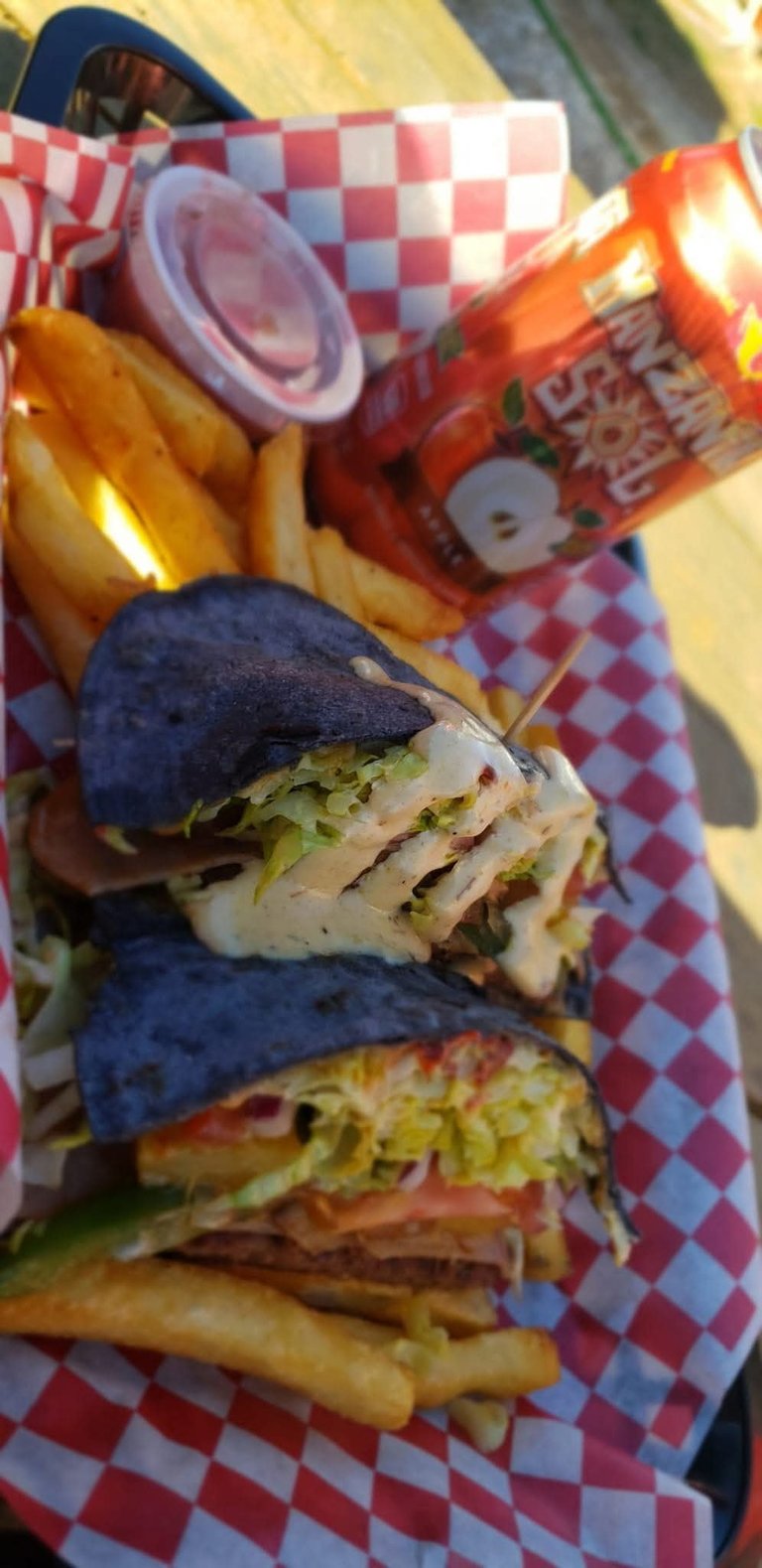 Charcoal buns sandwiches with lettuce and meat on red checkered paper with fries and sauce in background