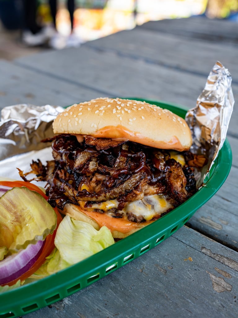 Pulled pork sandwich with melted cheese and caramelized onions on sesame bun, served with pickles and red onion on green tray