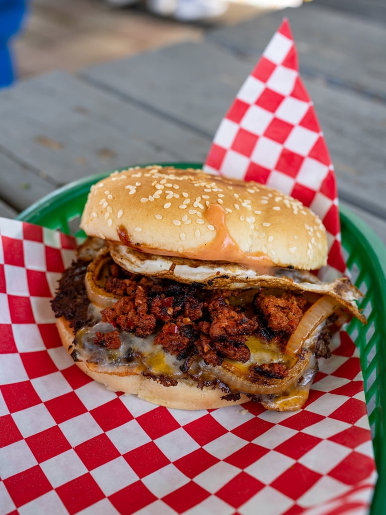 Gourmet burger with crispy fried onions and melted cheese on sesame bun, served on checkered paper in green basket