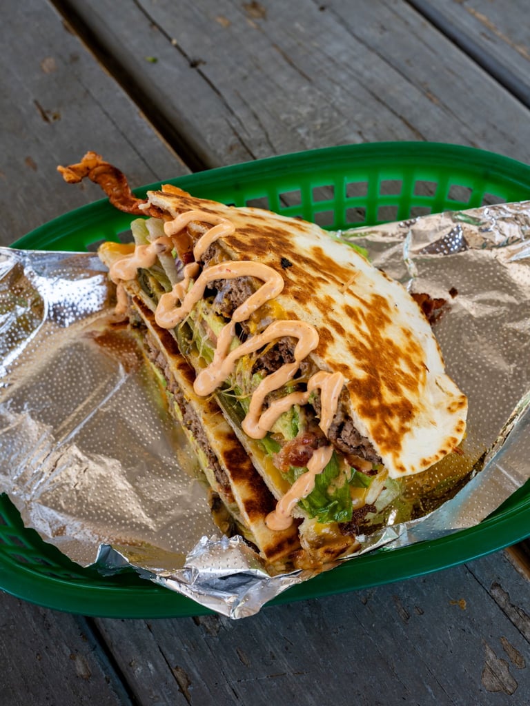 Crispy grilled taco on green plate with melted cheese, lettuce, and crispy onion strands on wooden surface