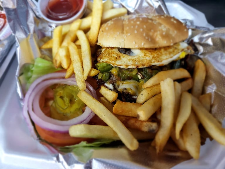 Gourmet burger with breaded chicken patty, greens, and onions served with French fries and jalapeño slices on a plate