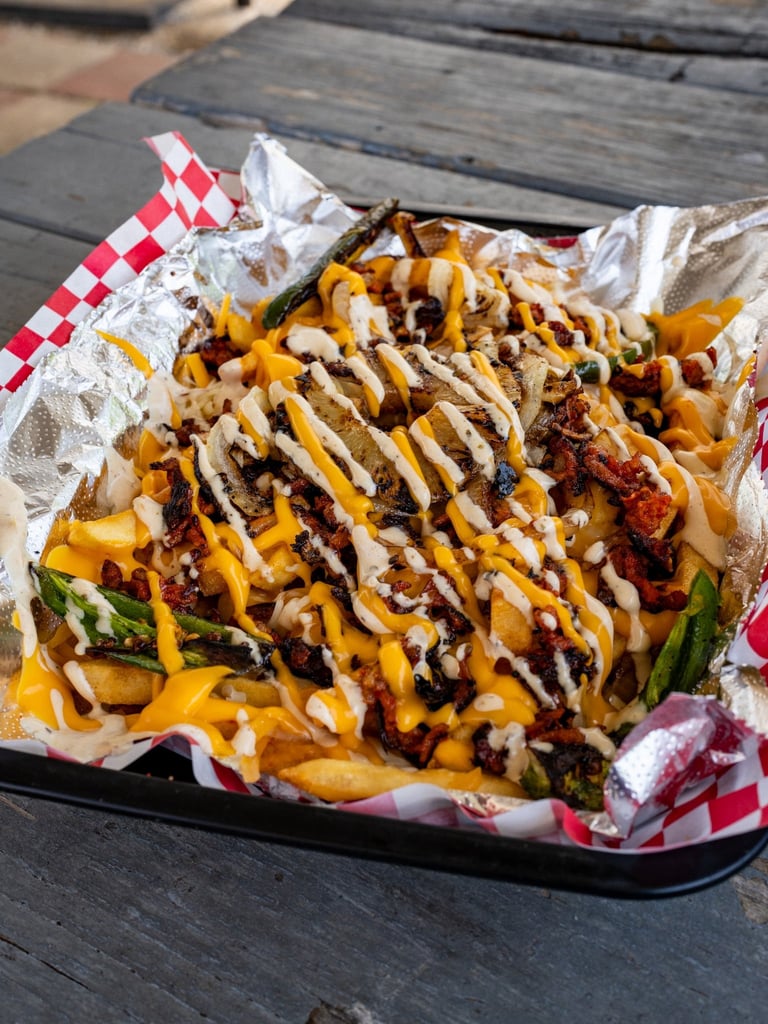Loaded french fries with melted cheese, meat, and drizzled sauces served in a red checkered paper boat