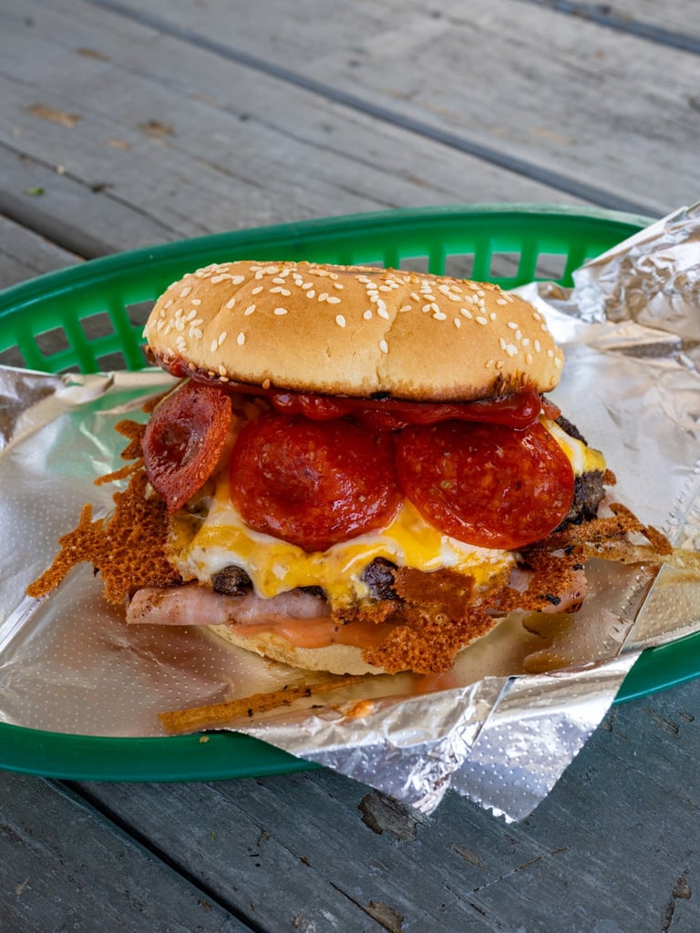 Fried chicken sandwich topped with melted cheese and pepperoni slices on a sesame seed bun in a green basket.